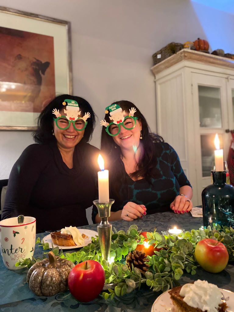 Twee vrouwen aan een kerstversierde tafel met een taartje en Who am I, Elf Glasses op. 