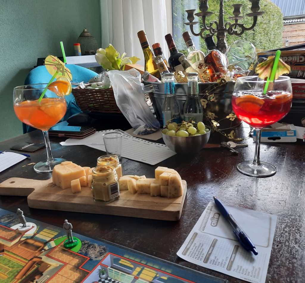 Tafel met het bordspel Cluedo, cocktails, kaasplankje en een schaal met druiven. 