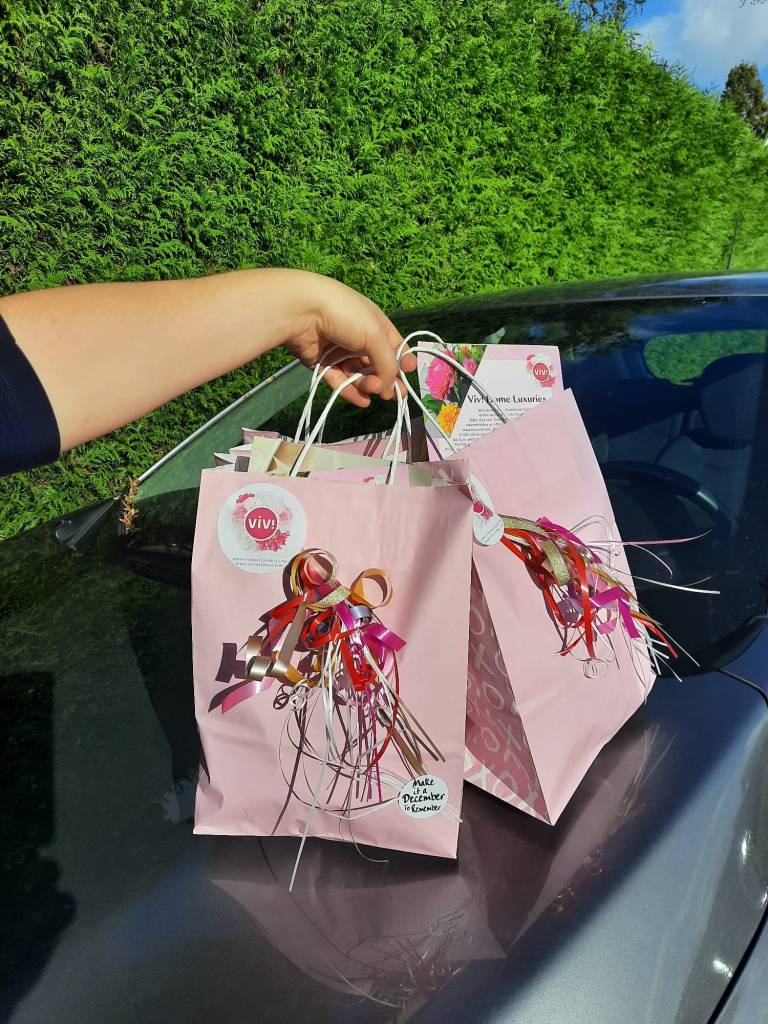 Een hand met twee roze shoppingtasjes van Viv! Christmas bovenop een motorkap