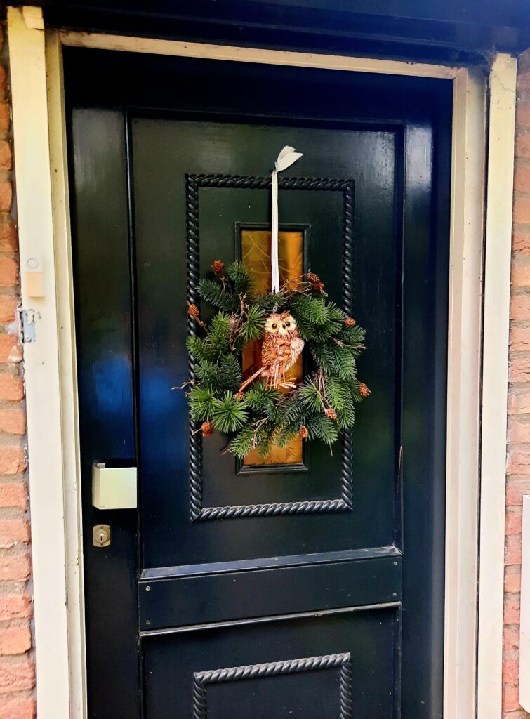 Groene deurkrans van dennegroen voor herfst en kerst, versierd met bruine dennenappels en een decoratieve uil.