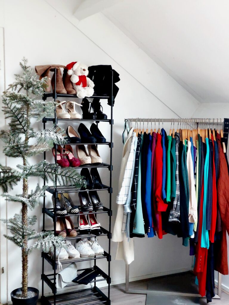 Minimalistische dressing room met schoenenrek vol hakken en laarzen, kleurrijk kledingrek en subtiele kerstdecoratie met besneeuwde kunstboom en teddybeer met kerstmuts.