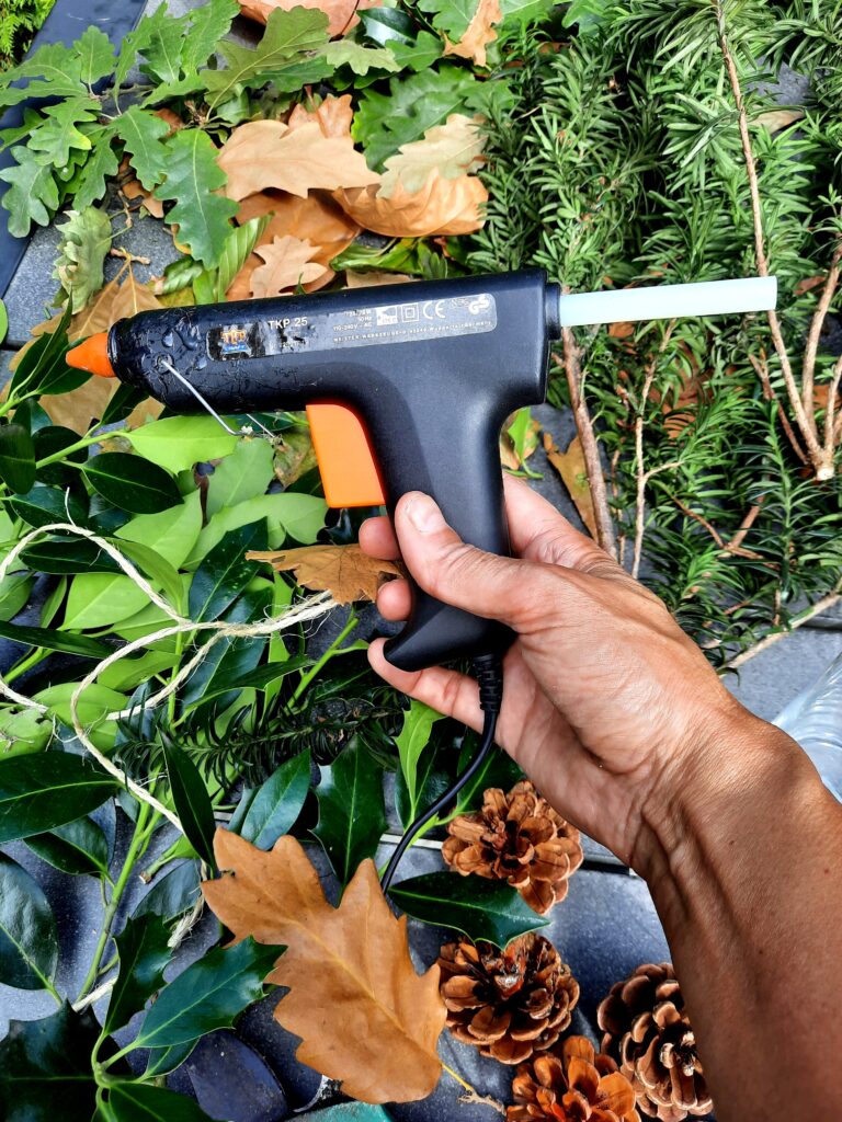 Lijmpistool en materialen voor DIY herfst- en kersttafelstuk met natuurlijke elementen