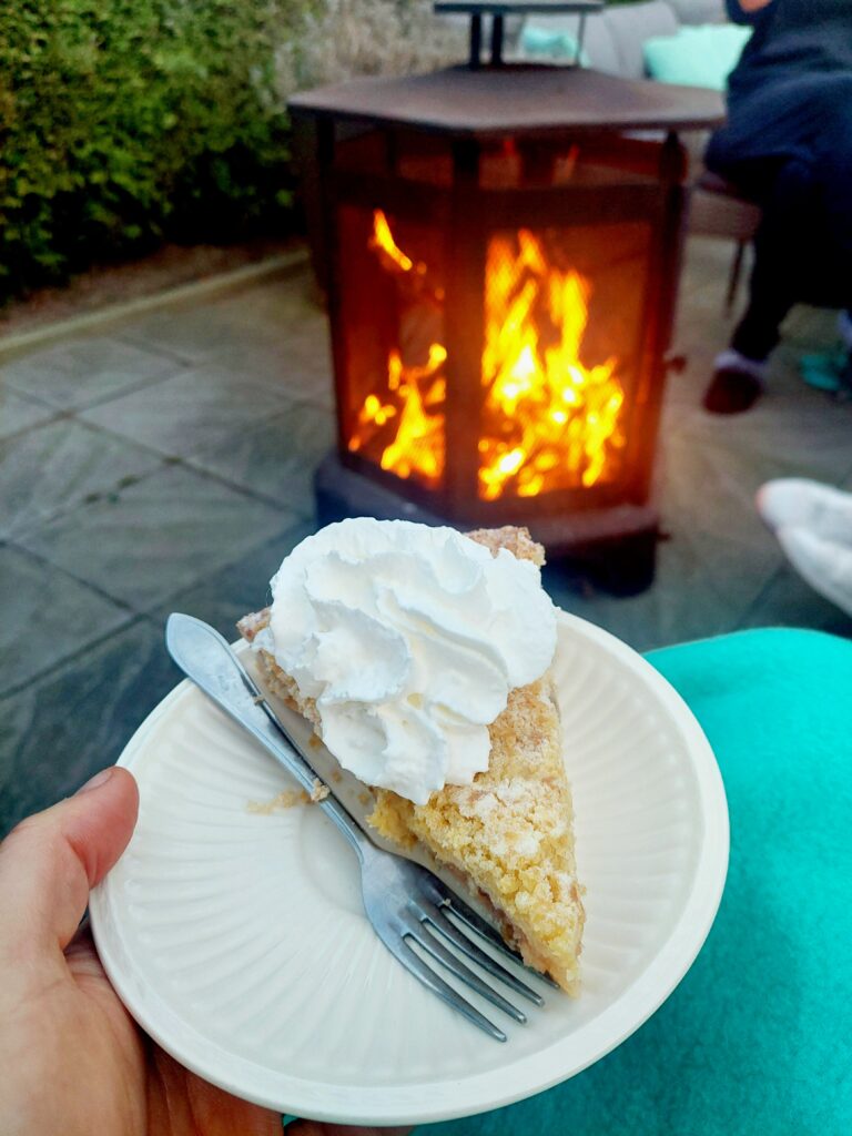 Bordje met een punt lemon pie en slagroom, op schoot met deken en vuurkorf op de achtergrond