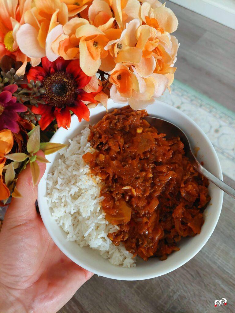 Surinaamse zuurkool in een witte kom met rijst naast herfstbloemen. 