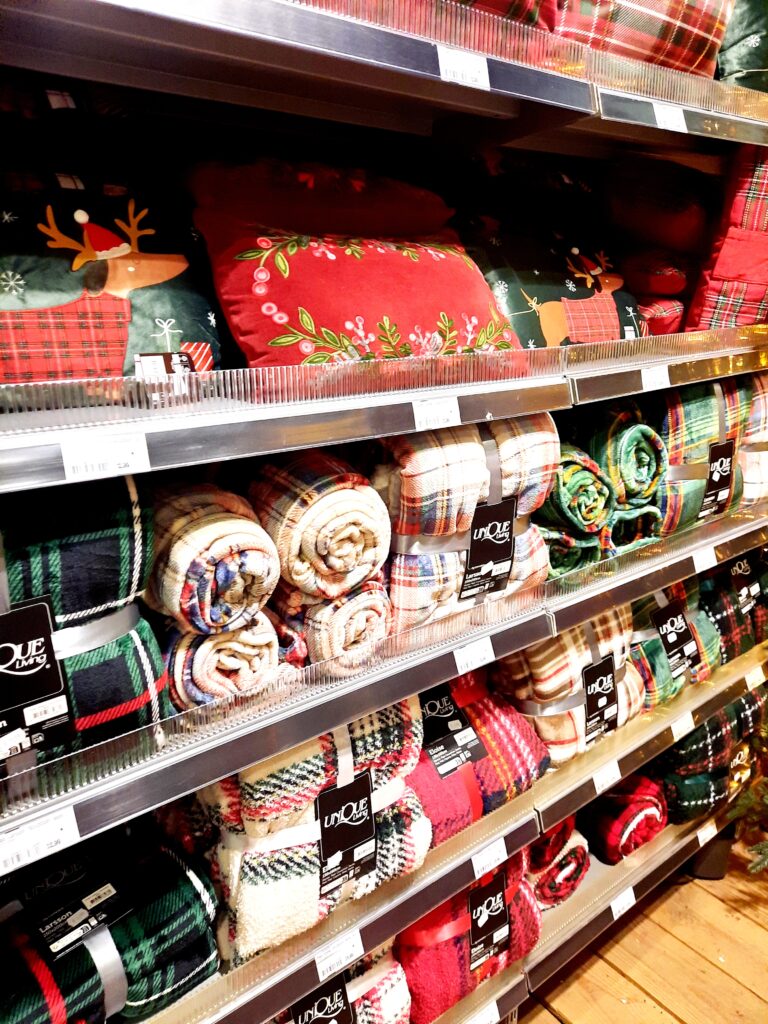 Wand met kerstkussens en warme dekens in tuincentrum, sfeervol gestyled met winterdecoratie.