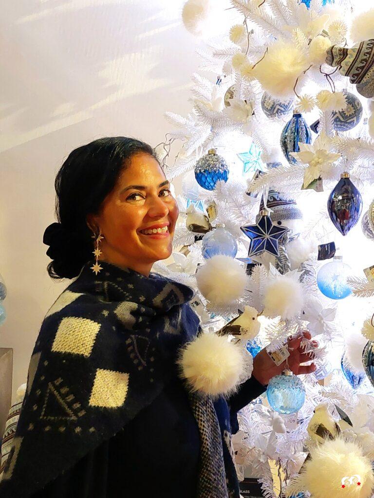Carmen voor een witte kerstboom met zacht witte en blauwe ornamenten, een donkerblauwe sjaal en ster oorbellen
