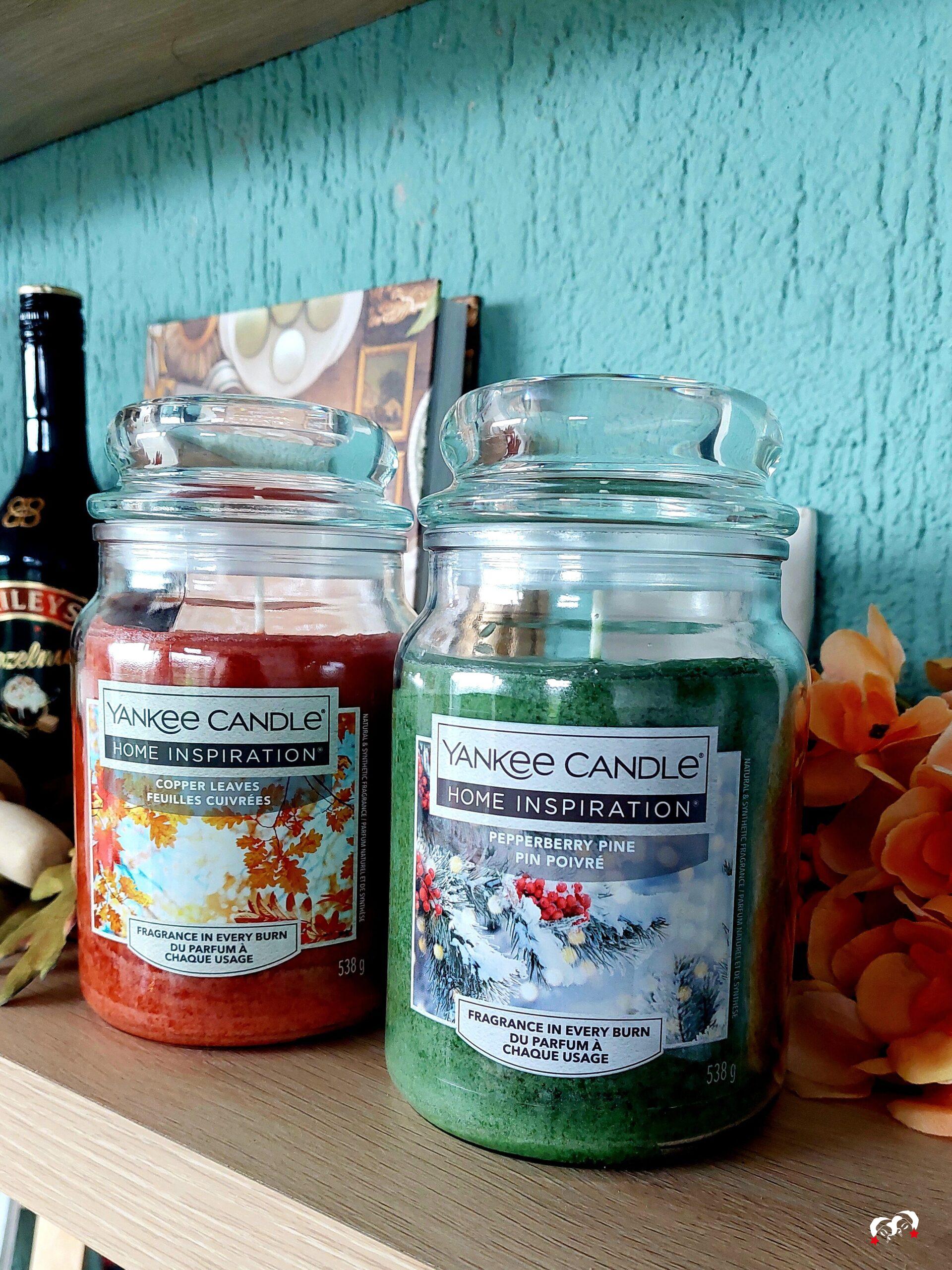 Twee geurkaarsen op een mantel met herfstdecoratie.