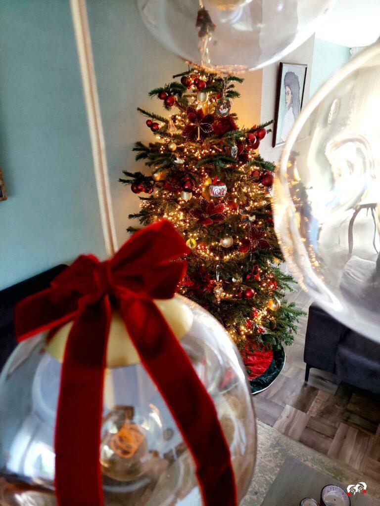 Kerstboom met burgundy rode en gouden ornamenten geschoten van bovenaf tussen bolvormige lampen.