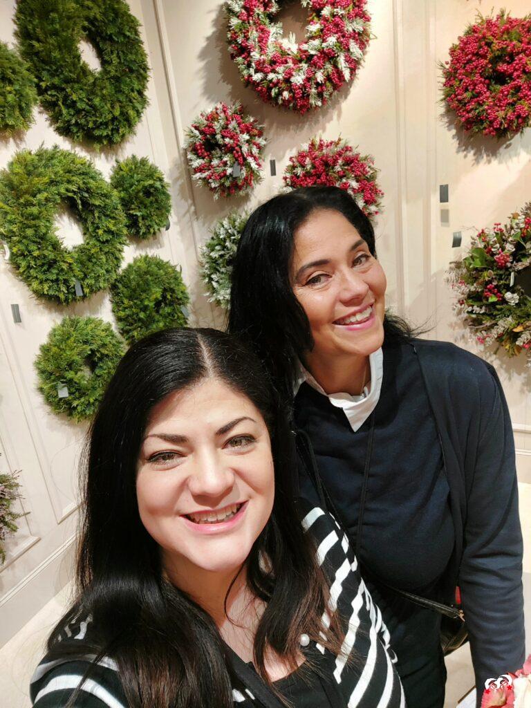 Yardéna en Carmen van The Christmas Girls poseren voor een muur met groene en bloemrijke kerstkransen