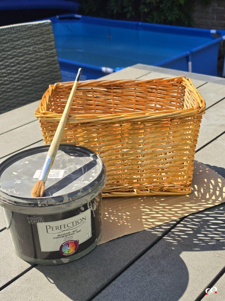 Tuintafel met een pot verf, kwast en mandje met op de achtergrond een zwembadje in de tuin.