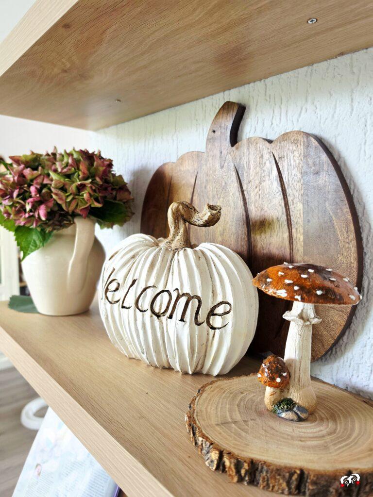 Landelijke herfstdecoratie op een wandplank met een witte pompoen, bordeaux hortensia’s en paddenstoelen.